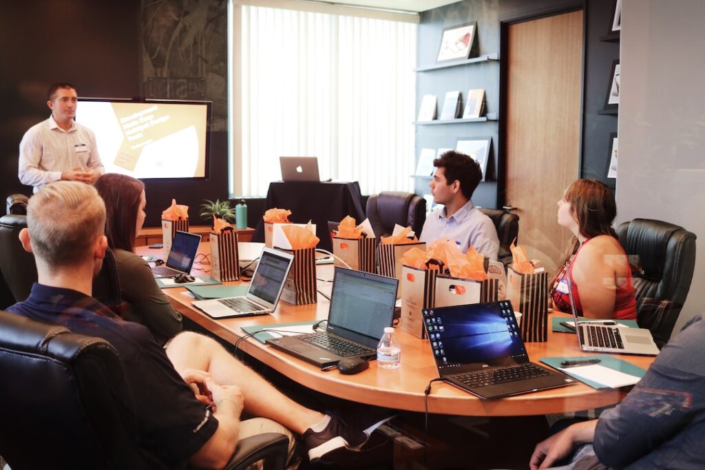 A manager discusses a sales enablement program with a team sitting at a table with laptops.